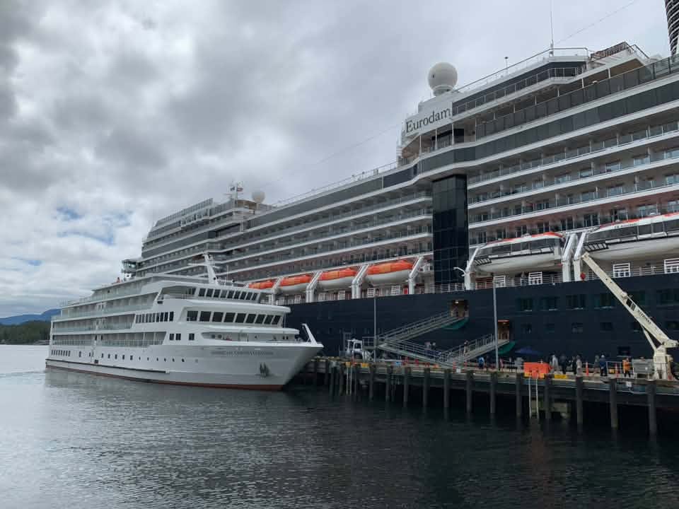 Small American Cruise Lines ship docked beside a much larger multi-deck cruise ship in Ketchikan, Alaska, showing the dramatic difference in ship size.